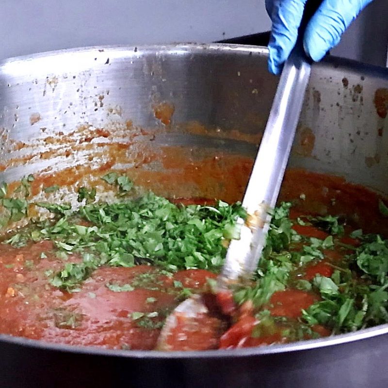 Preparazione artigianale del sugo Cuore Verde Natura: un operatore mescola a mano il condimento all'interno di una grande pentola in acciaio da 30kg.